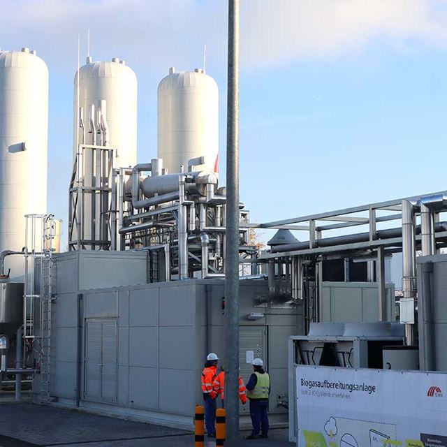 Seitliche Ansicht der Biogasaufbereitungsanlage mit davorstehenden Mitarbeitenden