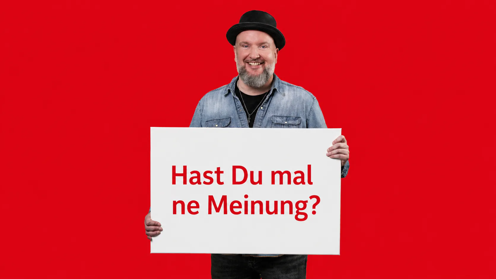 Unser Mitarbeiter Sebastian Lappe hält ein weißes Schild auf dem in Roter Farbe steht: Hast Du mal ne Meinung? Her Hintergrund ist ebenfalls rot.