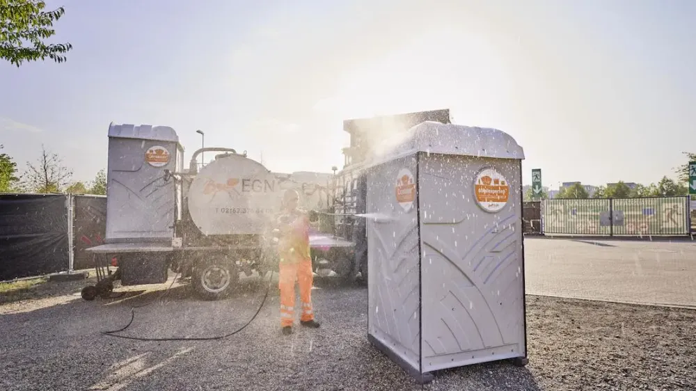 EGN Kollege reinigt eine mobile Toilette von außen mit einem Schlauch