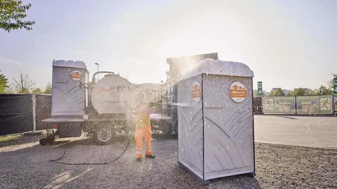 EGN Kollege reinigt eine mobile Toilette von außen mit einem Schlauch