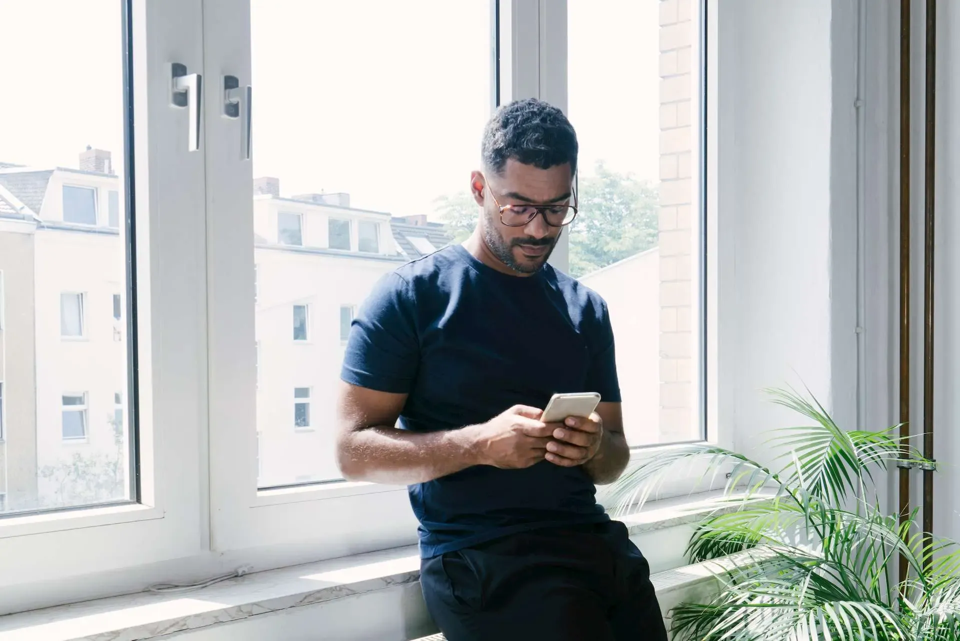 Mann lehnt an Fensterbank und schaut aufs Smartphone