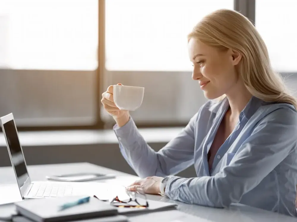 Junge Frau sitzt mit einer Tasse vor dem Laptop