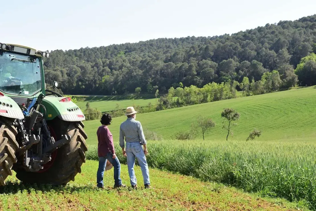Zwei Personen stehen vor Traktor auf einem Feld