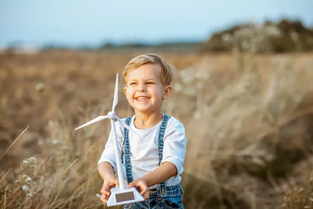 Kleiner Junge auf einem Feld spielt mit einem Spielzeugwindrad