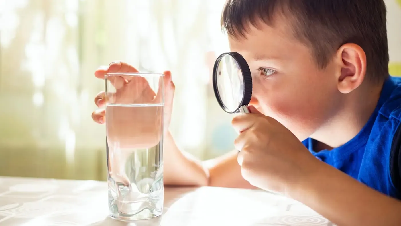Junge schaut sich Wasser im Glas mit einer Lupe an