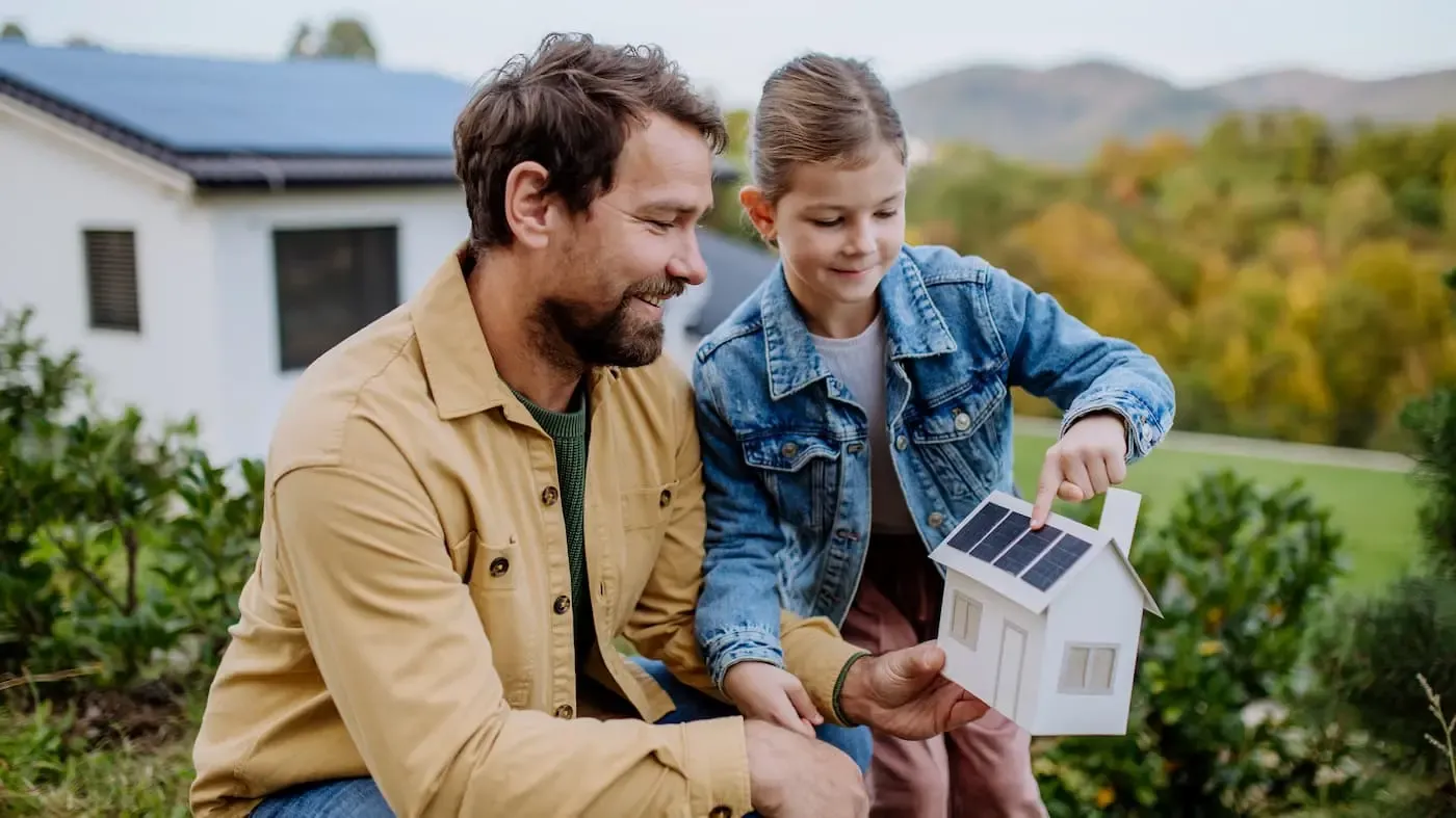 Vater zeigt seiner Tochter ein Modellhaus mit Photovoltaik auf dem Dach