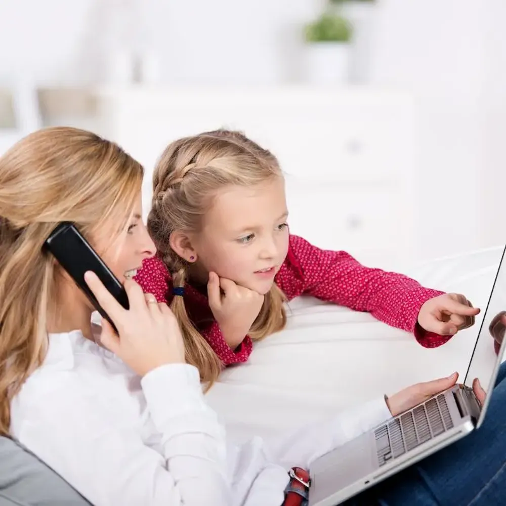 Mutter und Tochter schauen auf den Laptop und die Mutter telefoniert