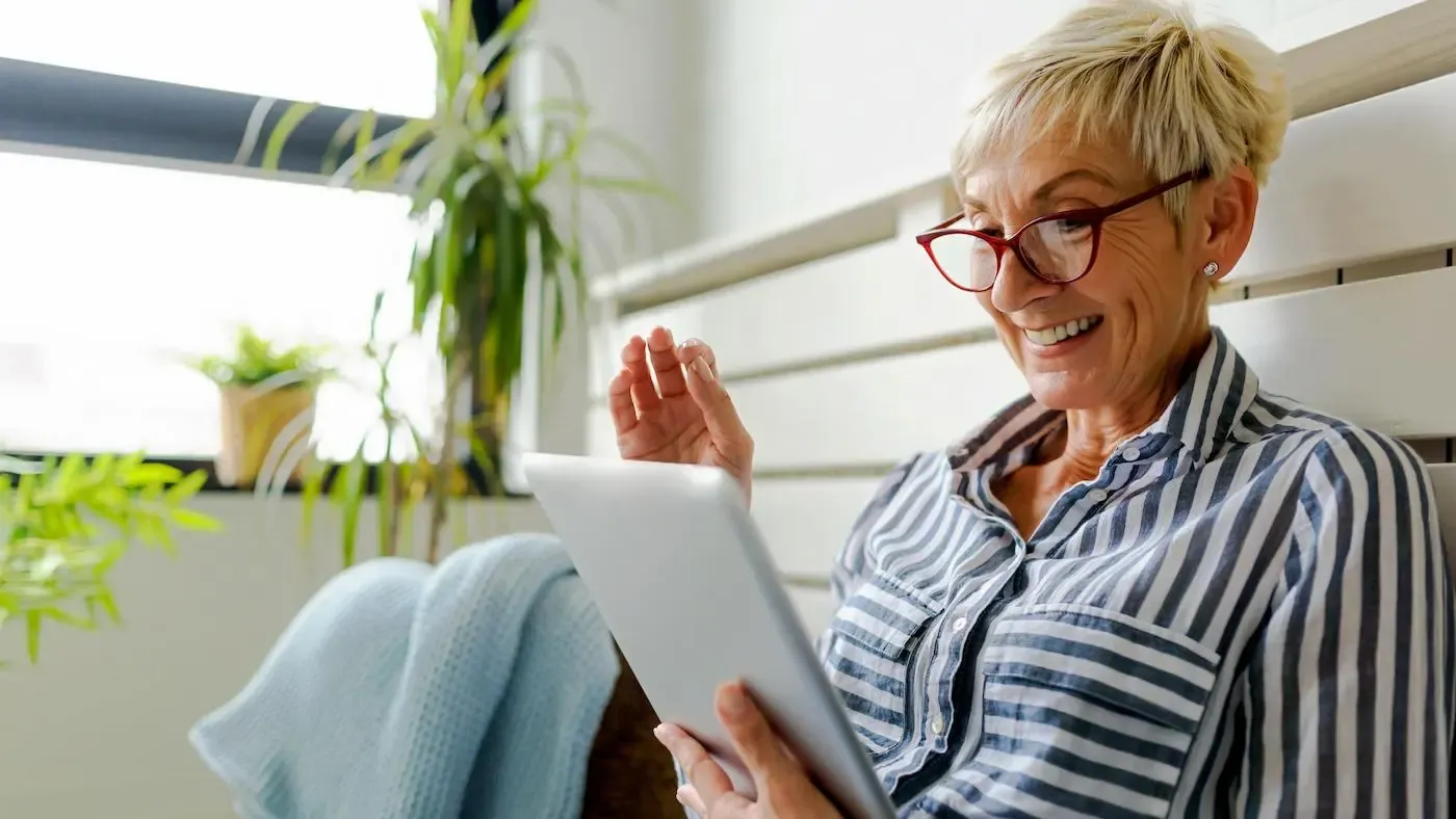 Frau sitzt vor Kommode und übermittelt über ihr Tablet einen Zählerstand