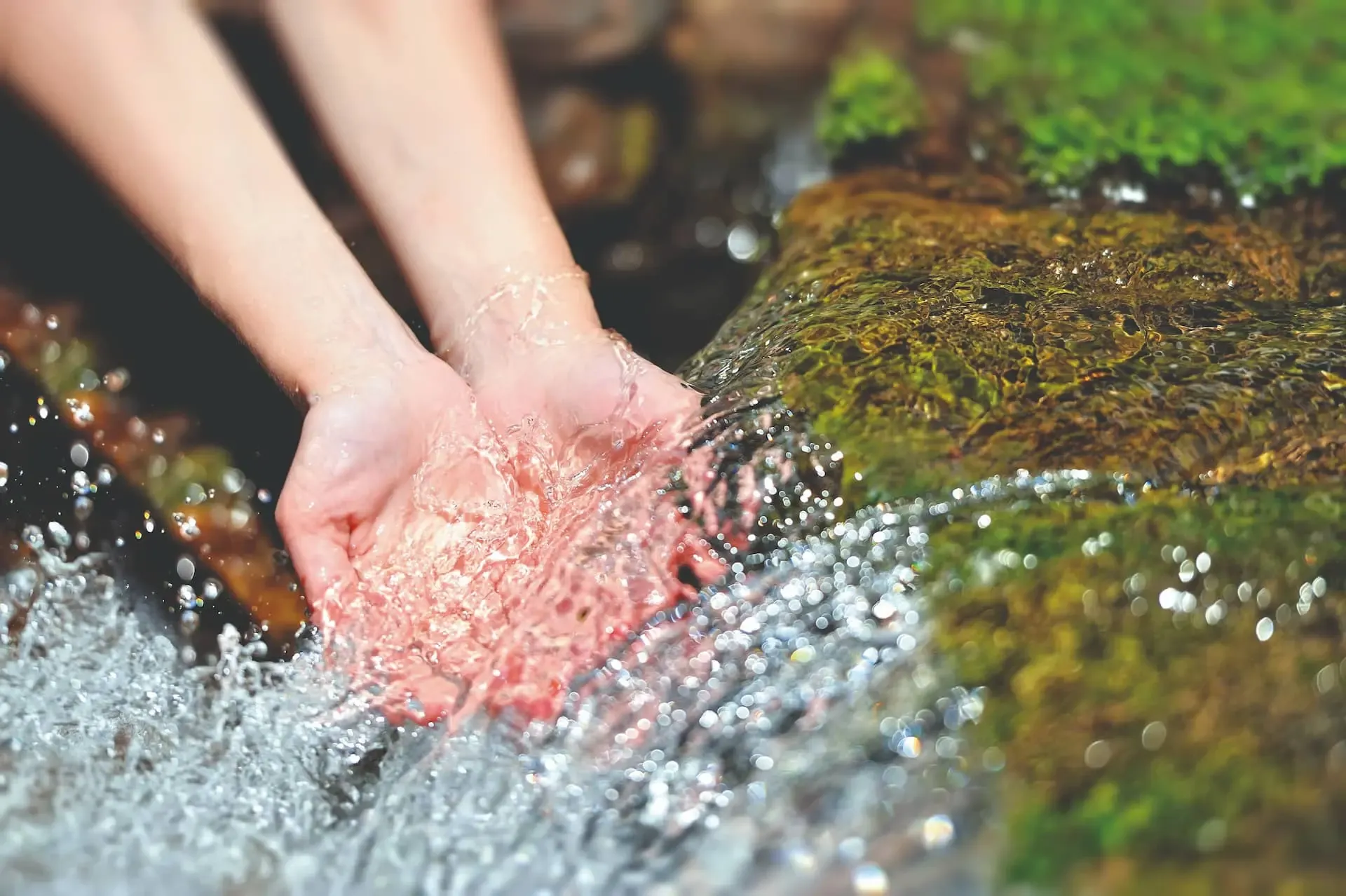 Hände fangen Wasser in einem Bach auf