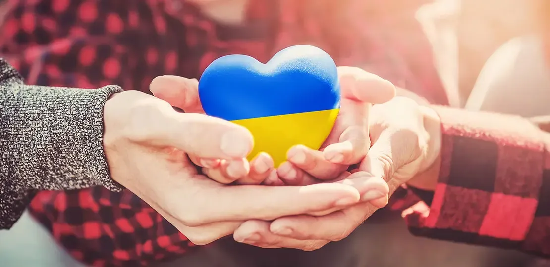 Mehrere Personen halten ein Herz in Ukraine Farben in der Hand