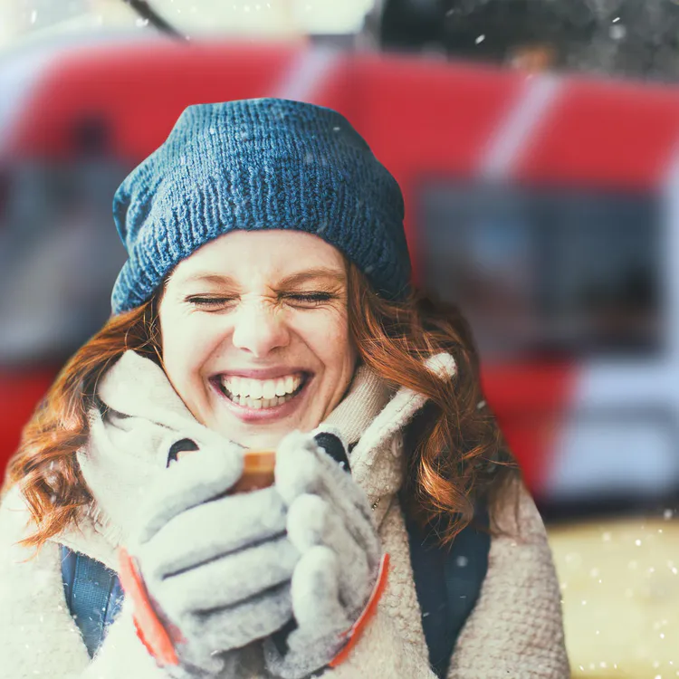 Frau mit Winterkleidung hat heißes Getränk in der Hand und ist glücklich, im Hintergrund ist eine Straßenbahn zu sehen