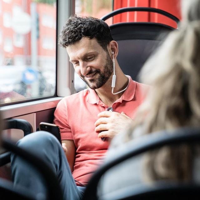 Mann sitzt im Bus und hört Musik mit Smartphone