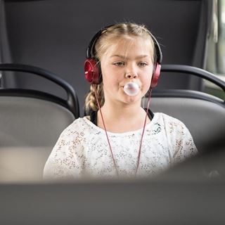 Mädchen sitzt im Bus und macht eine Kaugummi-Blase