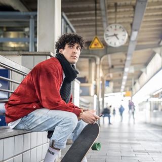 Jugendlicher sitzt mit Skateboard am Bahnsteig und wartet